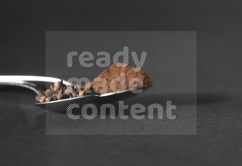 ملعقتان معدنيتان، إحداهما ممتلئة بحبوب القرنفل والأخرى ببودرة القرنفل، على خلفية سوداء