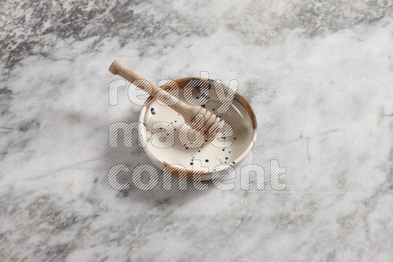 Multicolored pottery bowl with wooden honey dipper in it on grey marble background
