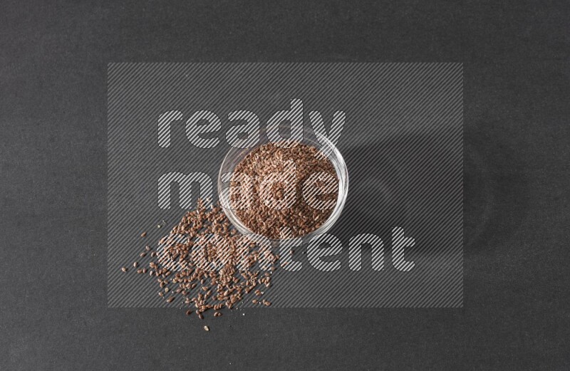 وعاء زجاجي ممتلئ بحبوب بذر الكتان محاط بالبذور على أرضية سوداء