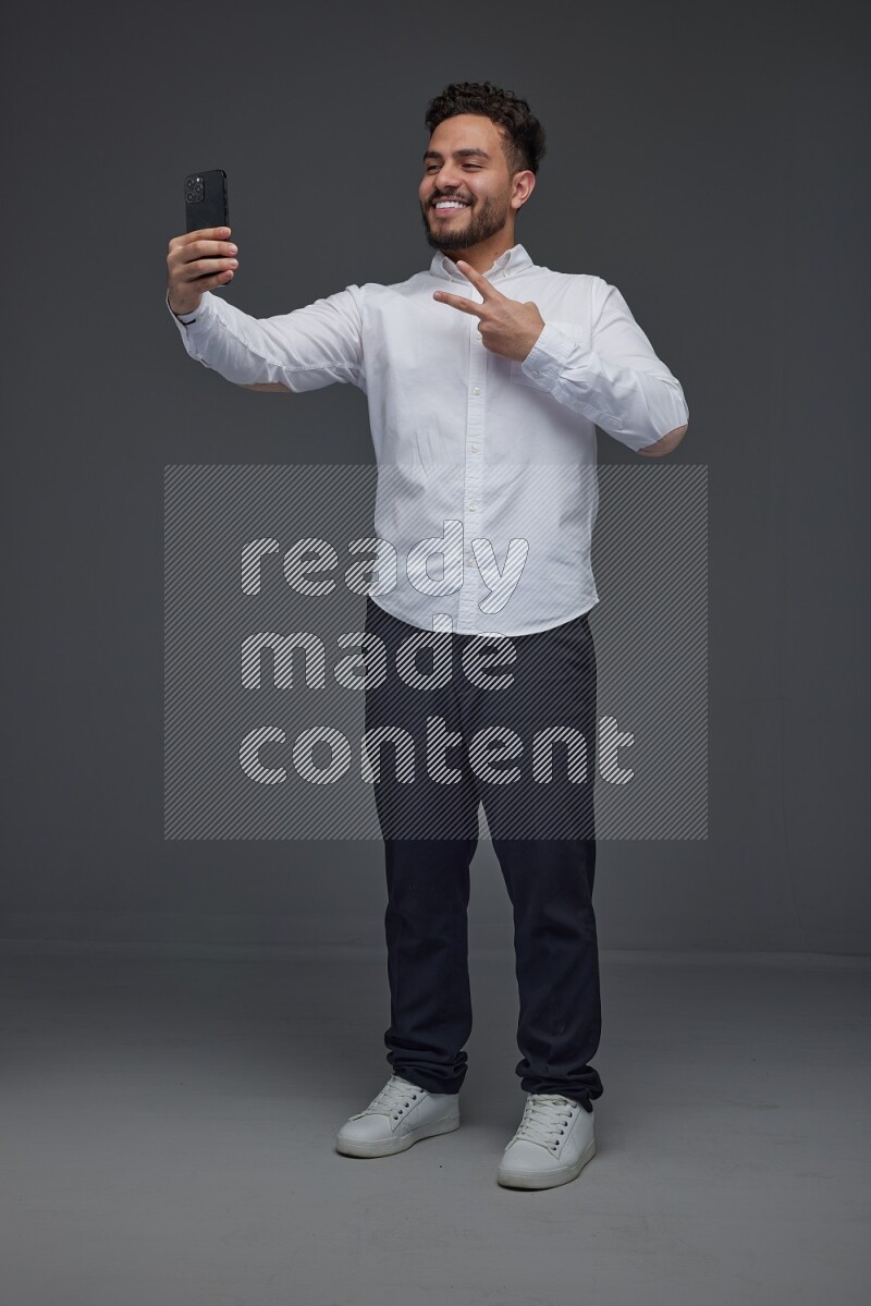 A man wearing smart casual and taking selfie with his phone eye level on a gray background