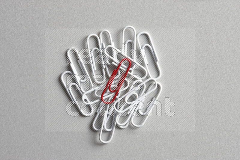 A red paperclip surrounded by bunch of white paperclips on grey background