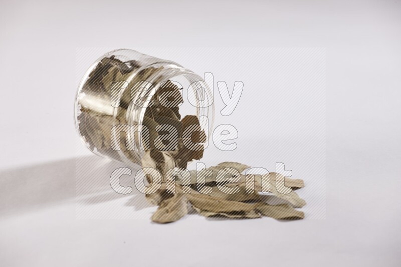 وعاء زجاجي ممتلئ بأوراق الغار والوعاء مقلوب وبعض الأوراق متناثرة خارجه علي خلفية بيضاء