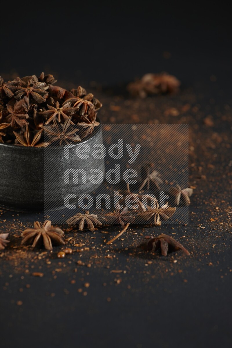 Star Anise in a black bowl with sprinkled anise on black flooring