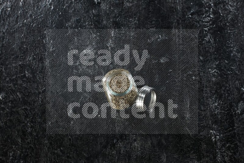 وعاء زجاجي للتوابل ممتلئ بحبوب الكمون على خلفية سوداء