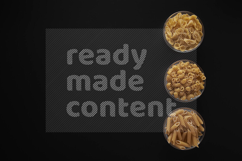 Different pasta types in 3 glass bowls on black background