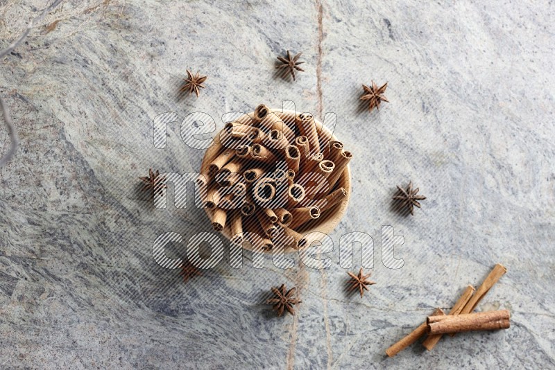wooden bowl full of cinnamon sticks surrounded by star anis on marble background in different angles