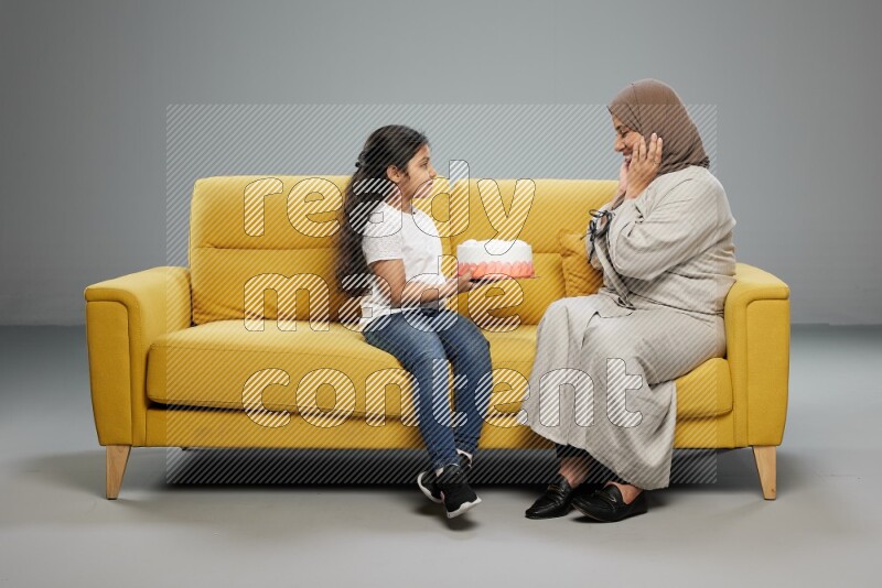 A girl sitting giving a cake to her mother on gray background