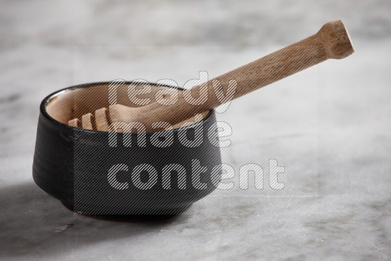 Black pottery bowl with wooden honey dipper in it on grey marble background