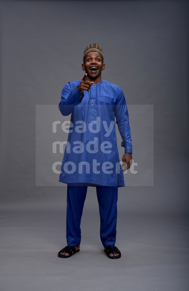Man wearing Nigerian outfit standing interacting with the camera on gray background