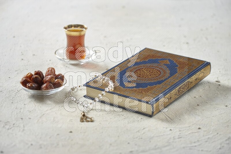 Quran with dates, prayer beads and different drinks all placed on textured white background