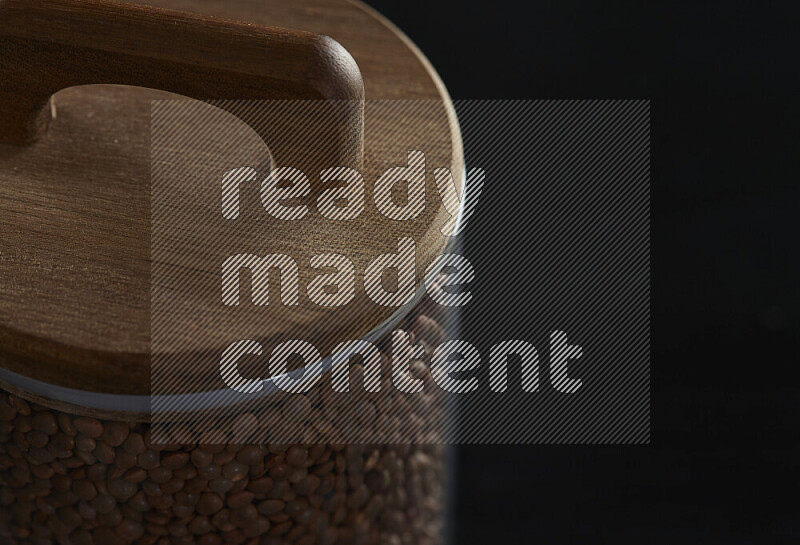 Brown lentils in a glass jar on black background