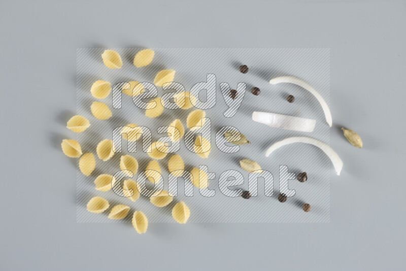 Raw pasta with different ingredients such as cherry tomatoes, garlic, onions, red chilis, black pepper, white pepper, bay laurel leaves, rosemary, cardamom and mushrooms on light blue background