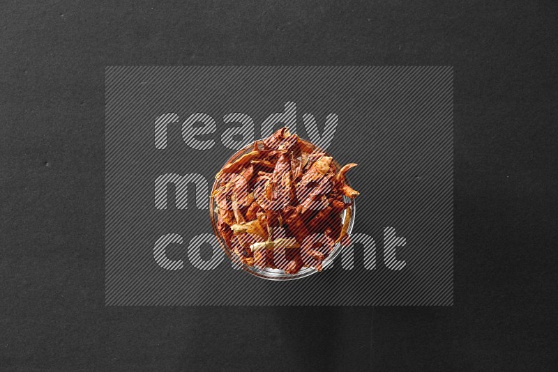 A glass bowl full of dried red chili peppers on black flooring