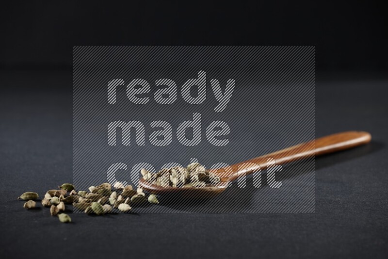 A wooden ladle full of cardamom on black flooring