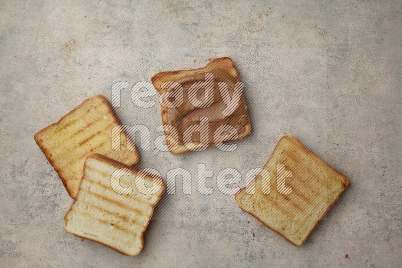 Creamy peanut butter on a toasted white toast and toasted white toast slices on a light blue textured background