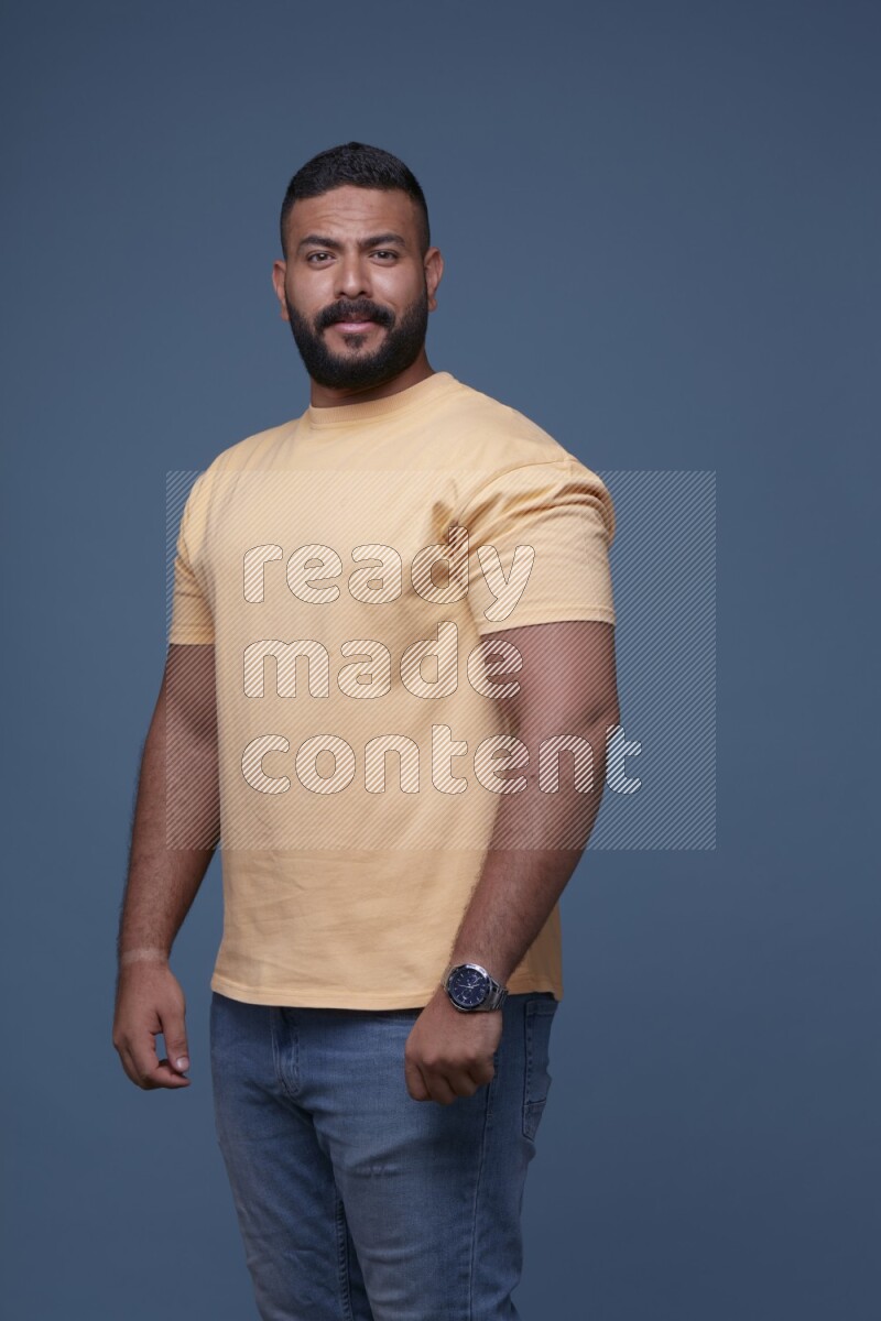 A man posing in a blue background wearing a yellow shirt