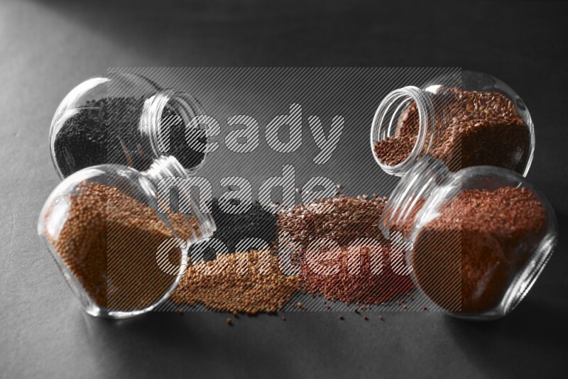4 glass spice jars full of black seeds, mustard seeds, flax and garden cress on black flooring