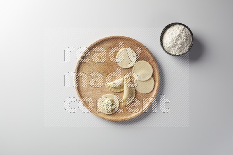 two closed sambosas and one open sambosa filled with cheese while flour aside in a wooden dish on a white background