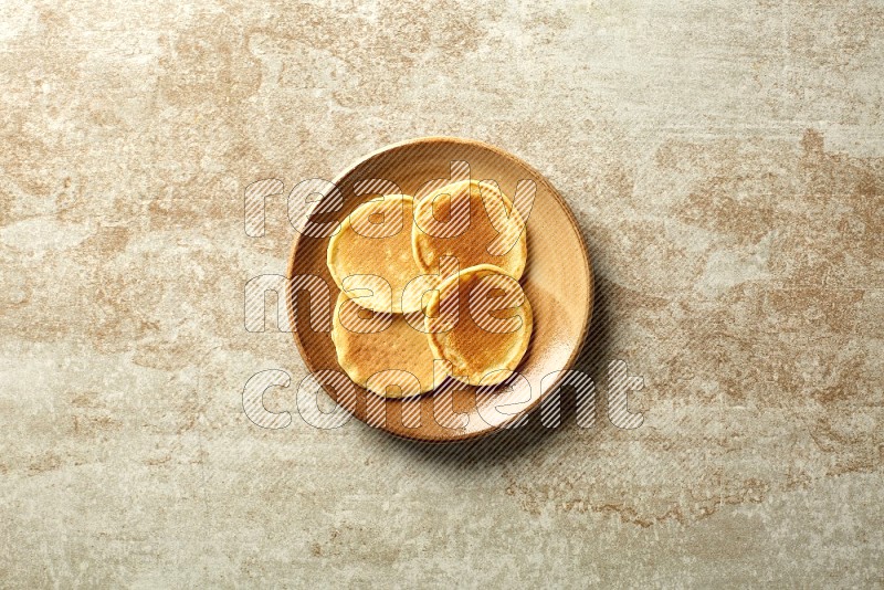 Four stacked plain mini pancakes in a brown plate on beige background