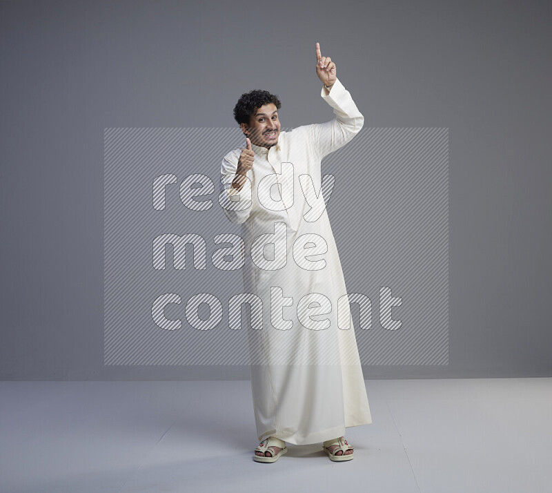 A Saudi man standing wearing thob interacting with the camera on gray background