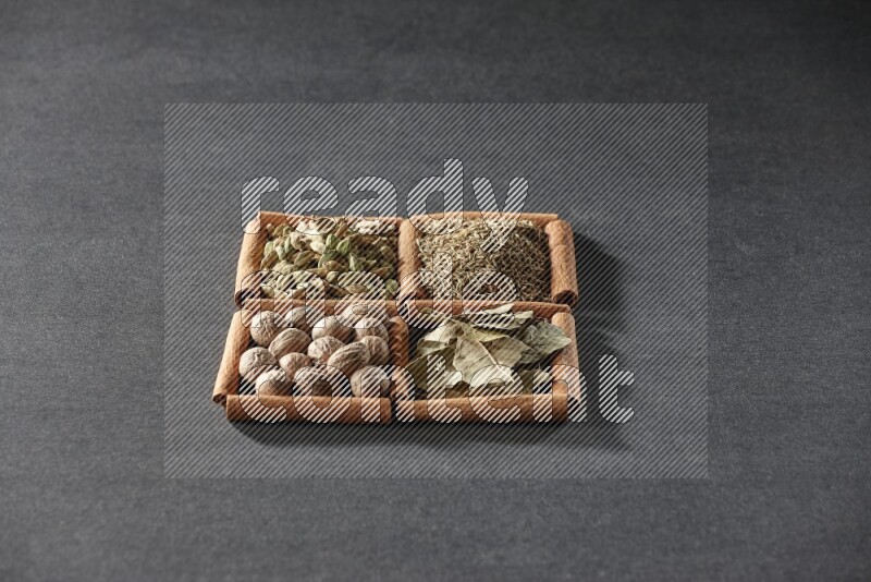 4 مربعات من عيدان القرفة ممتلئة بالكمون وحبوب الهيل وأوراق الغار وجوزة الطيب على أرضية سوداء