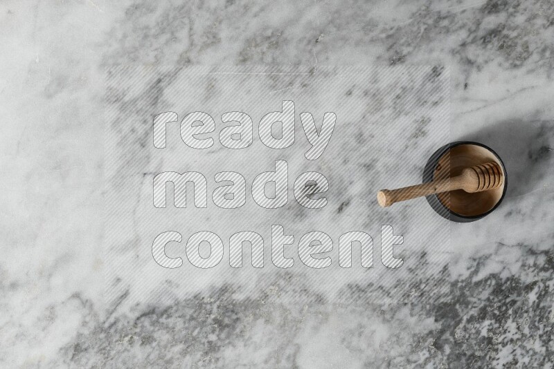 وعاء فخاري أسود مع ملعقة عسل خشبية بداخله على خلفية من الرخام الرمادي