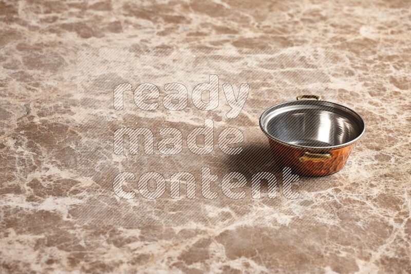 A small copper pot on beige marble background