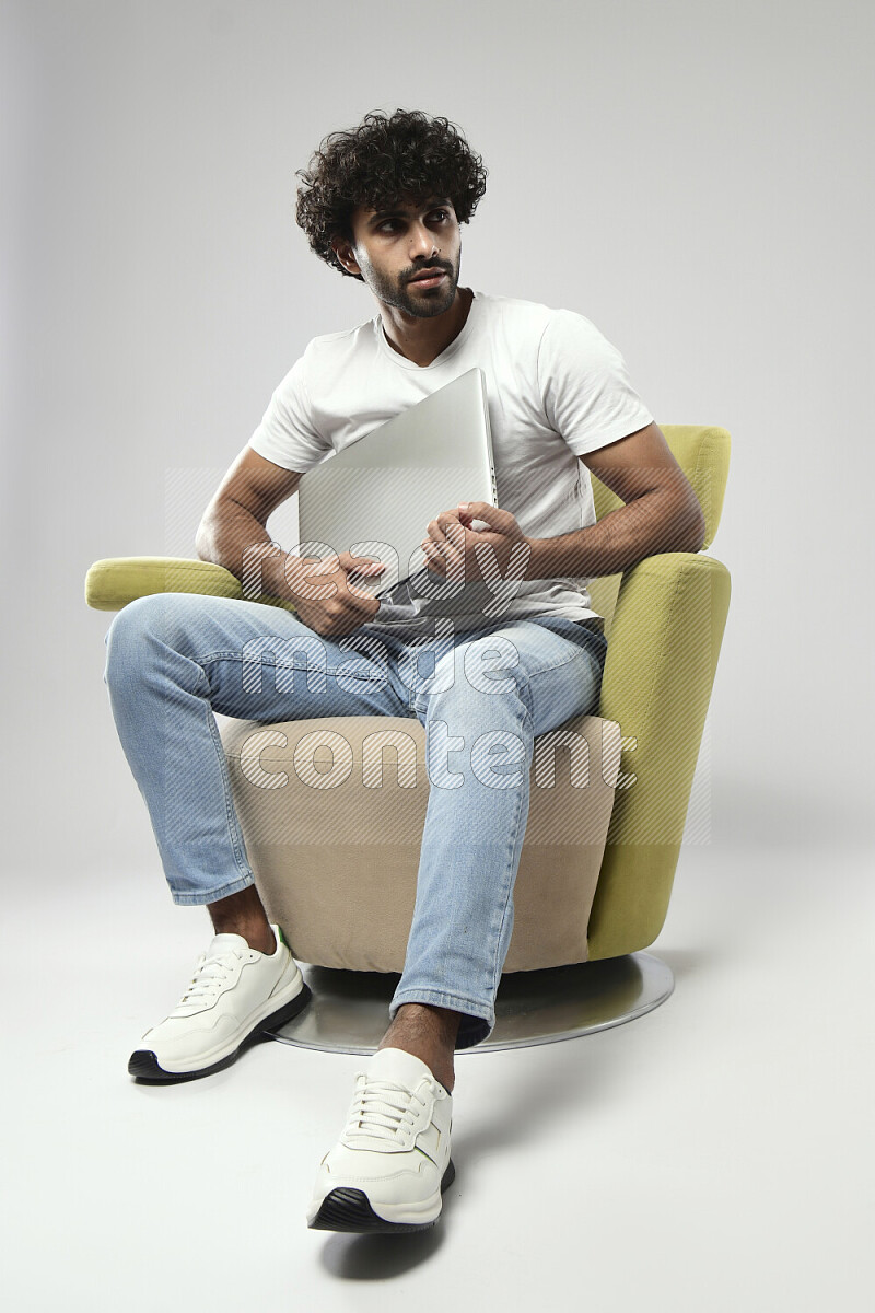 A man wearing casual sitting on a chair holding a laptop on white background