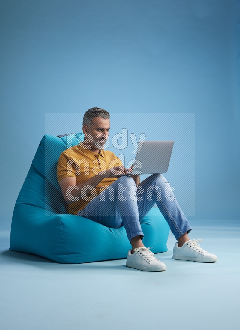 A man sitting on a blue beanbag and working on laptop