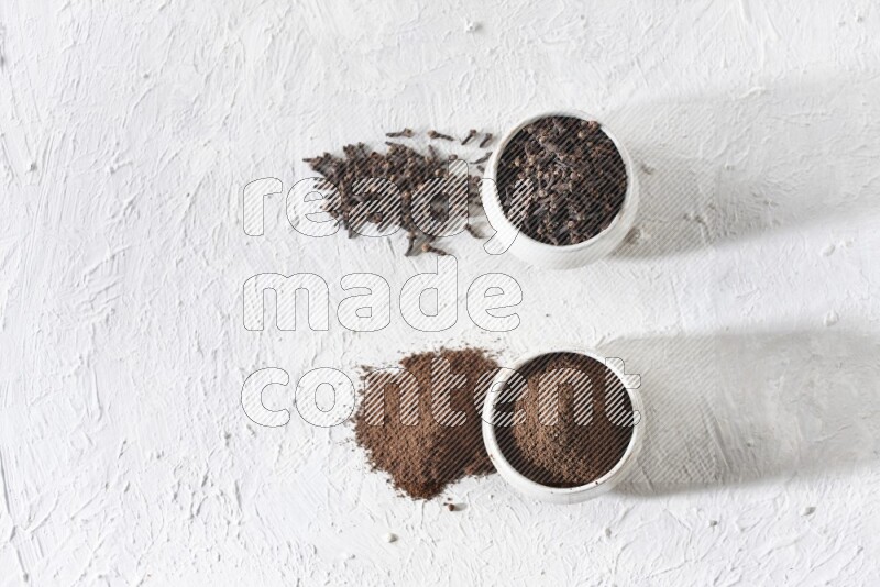 2 Beige ceramic bowls, one full of cloves and the other full of powder on textured white flooring