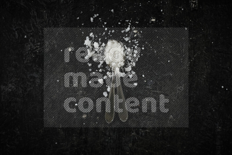 ملعقتان معدنيتان ممتلئتان بالملح الأبيض على خلفية سوداء