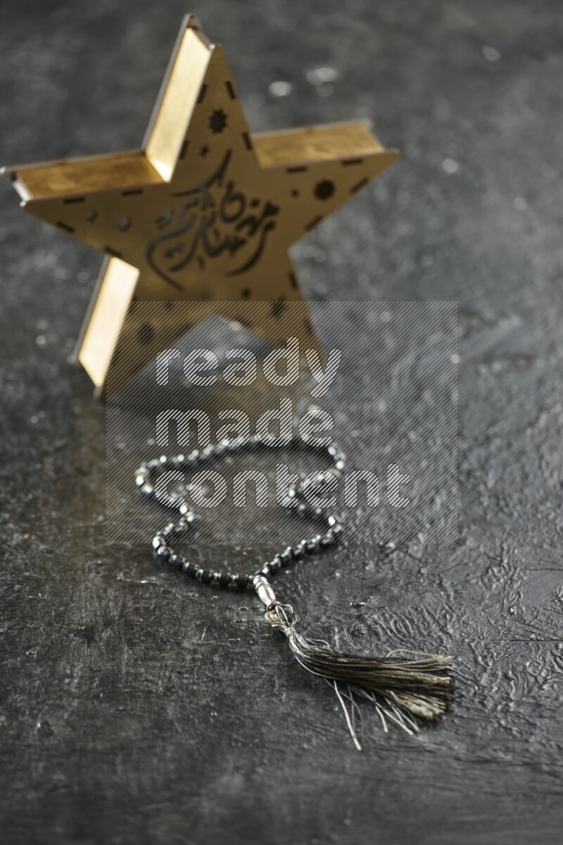 فانوس خشبي نجمي باللون الذهبي مع مشروبات مختلفة وتمر ومكسرات وسبحة صلاة وقرآن على خلفية سوداء