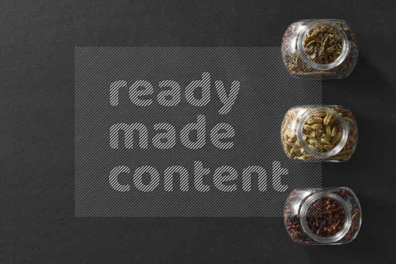 قرنفل وحبوب الهيل و ريحان مجفف في أوعية زجاجية علي خلفية سوداء