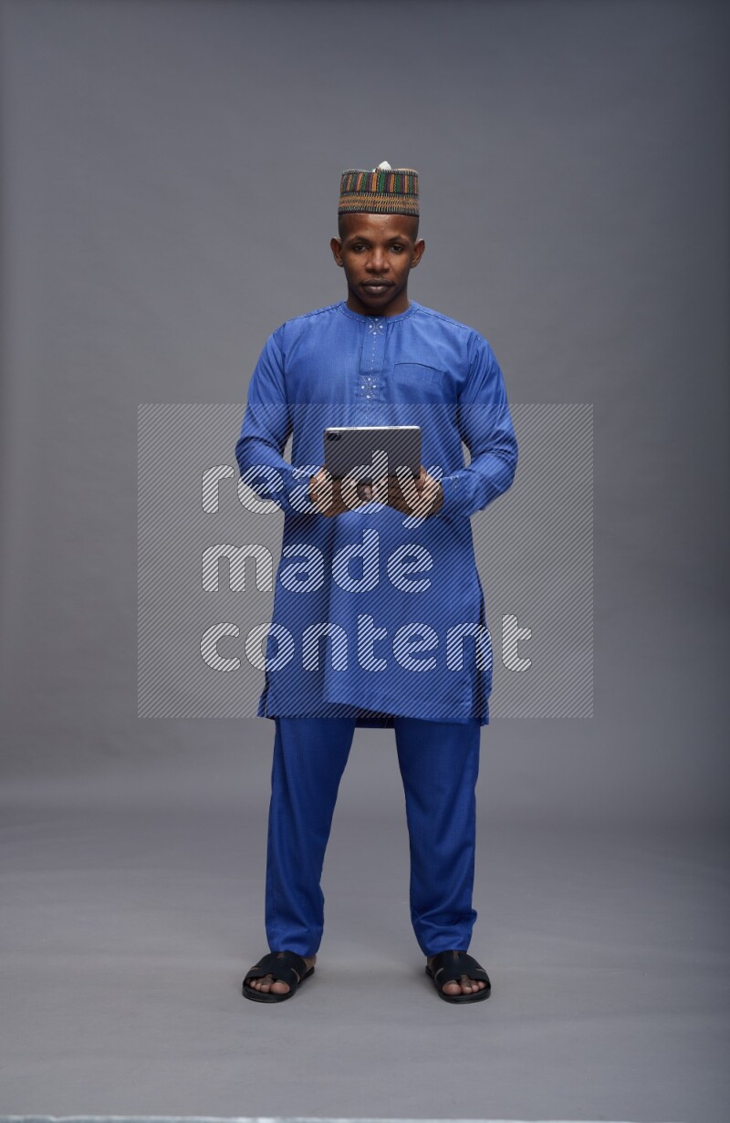 Man wearing Nigerian outfit standing working on tablet on gray background