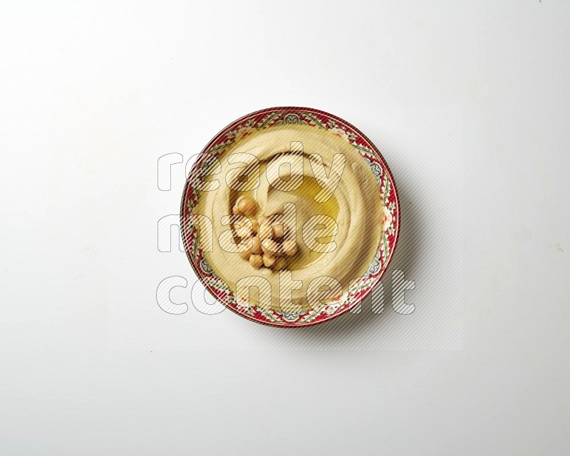 Hummus in a red plate with patterns garnished with roasted chickpeas  on a white background