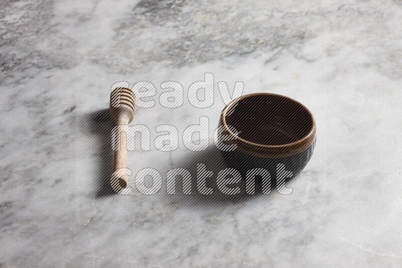 Multicolored pottery bowl with wooden honey dipper on the side on grey marble background