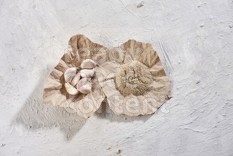 2 crumpled piece of paper full of garlic cloves and powder on a textured white flooring in different angles