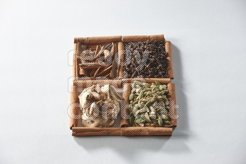 4 مربعات من أعواد القرفة ممتلئة بالهيل والقرفة والقرنفل والزنجبيل المجفف على أرضية بيضاء