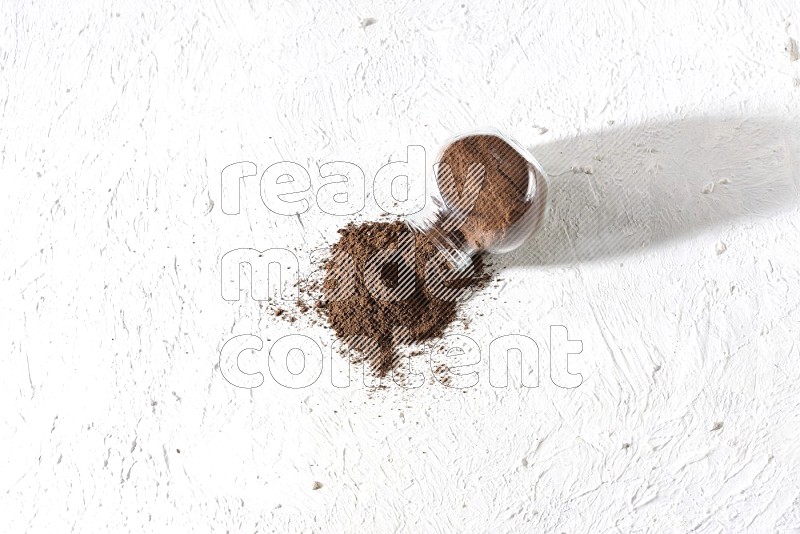 A flipped glass spice jar full of cloves powder and powder came out of it on textured white flooring