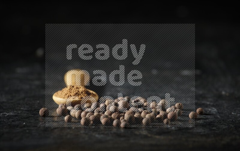 ملعقة خشبية ممتلئة ببودرة بهار الفلفل الحلو بجانب حبوب من الفلفل على خلفية سوداء