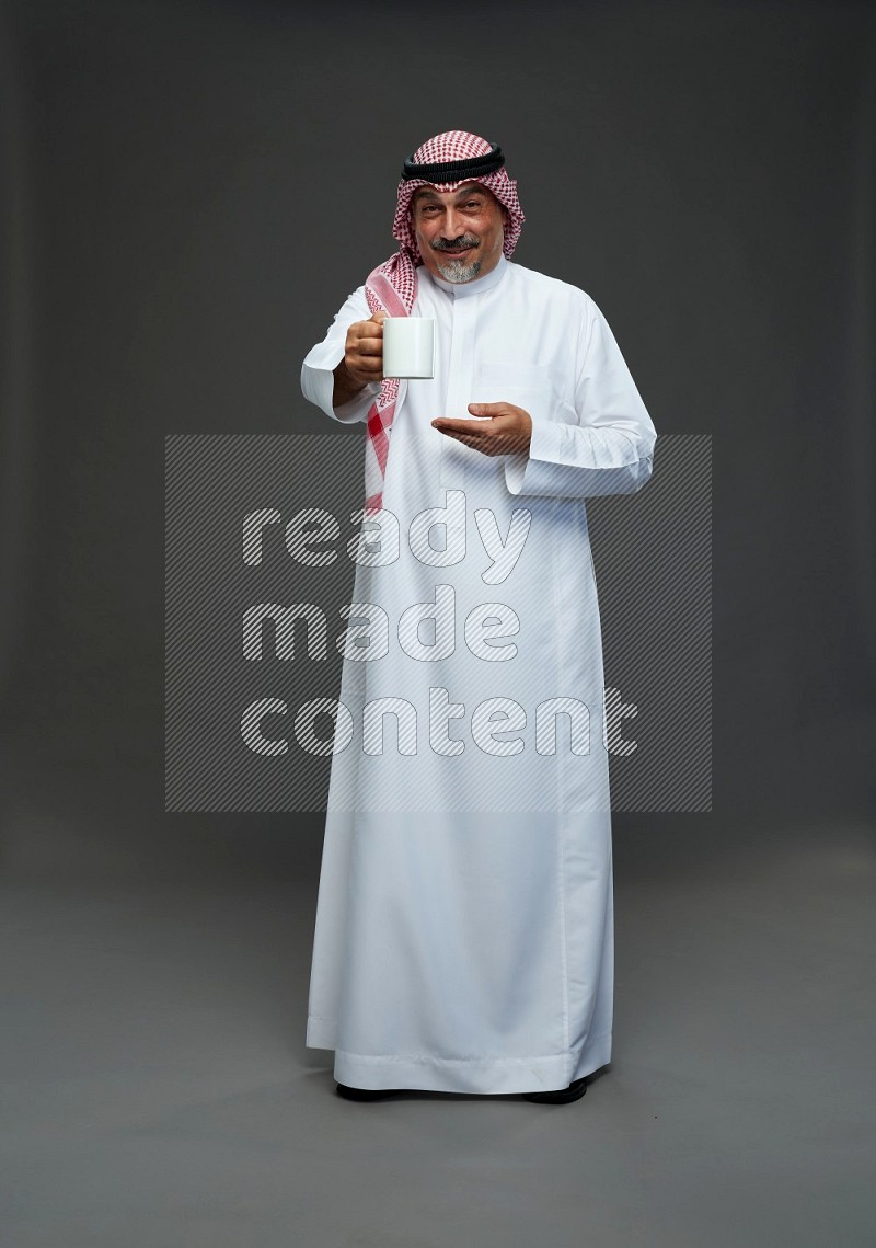 Saudi man with shomag Standing holding mug on gray background