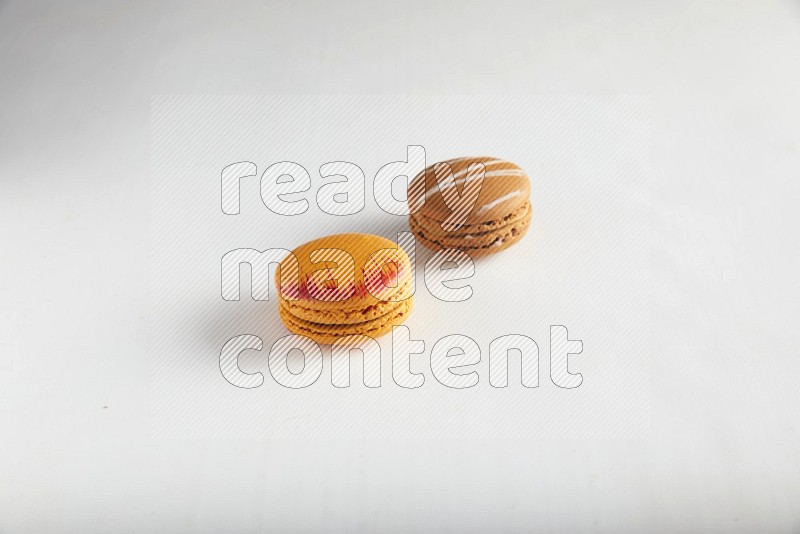 45º Shot of of two assorted Brown Irish Cream, and Orange Exotic macarons on white background