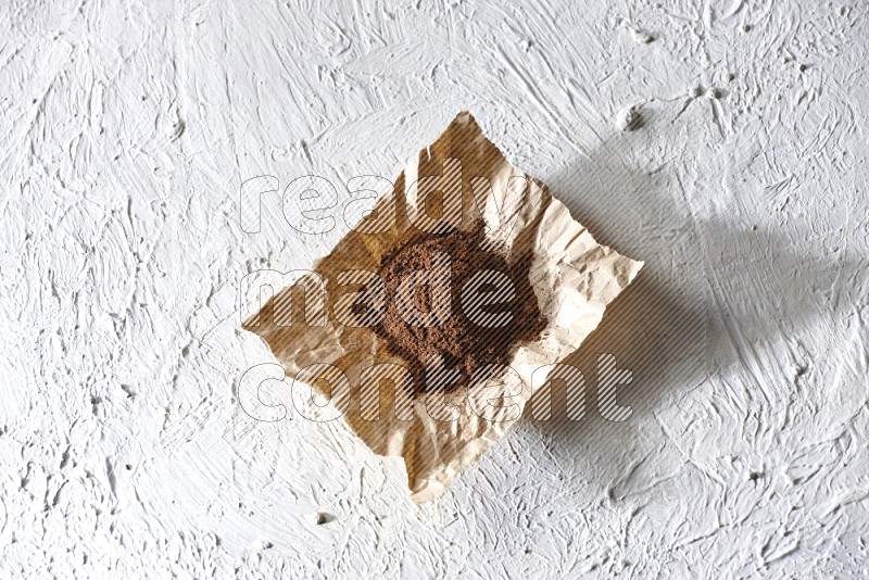 Cloves powder on crumpled piece of paper on a textured white flooring