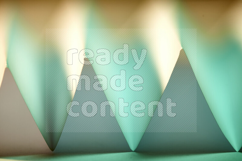 A close-up abstract image showing sharp geometric paper folds in green gradients and warm tones