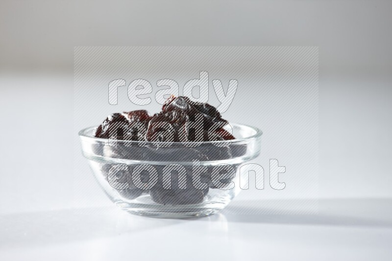 A glass bowl full of dried plums on a white background in different angles