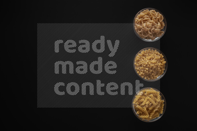 Different pasta types in 3 glass bowls on black background