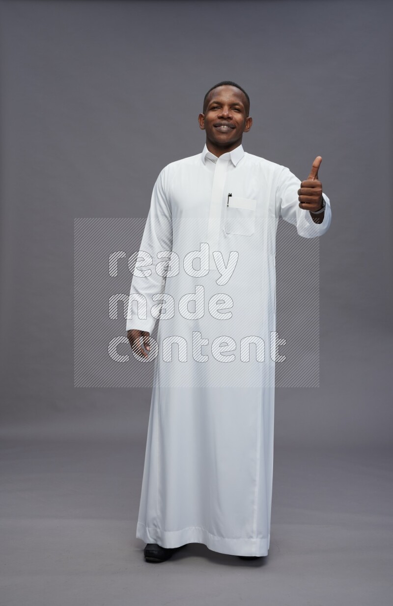 Saudi man wearing thob standing interacting with the camera on gray background