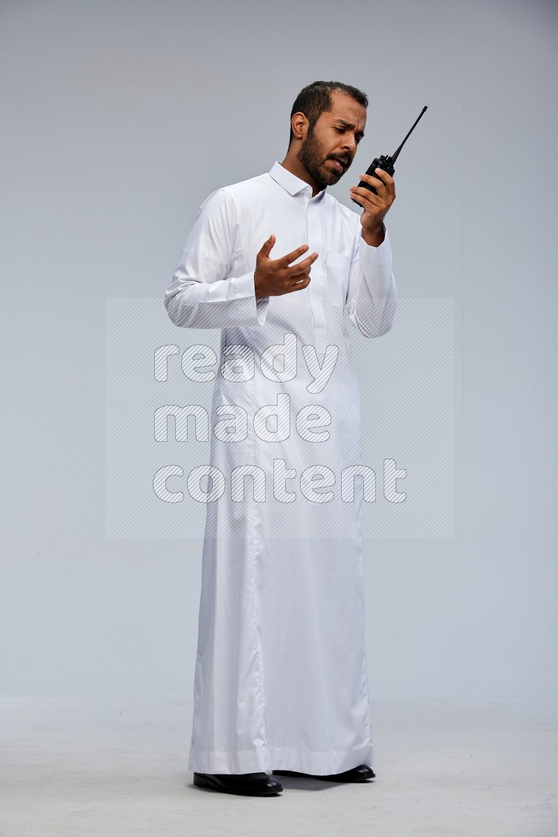 Saudi man Wearing thob standing holding walkie-talkie on Gray background