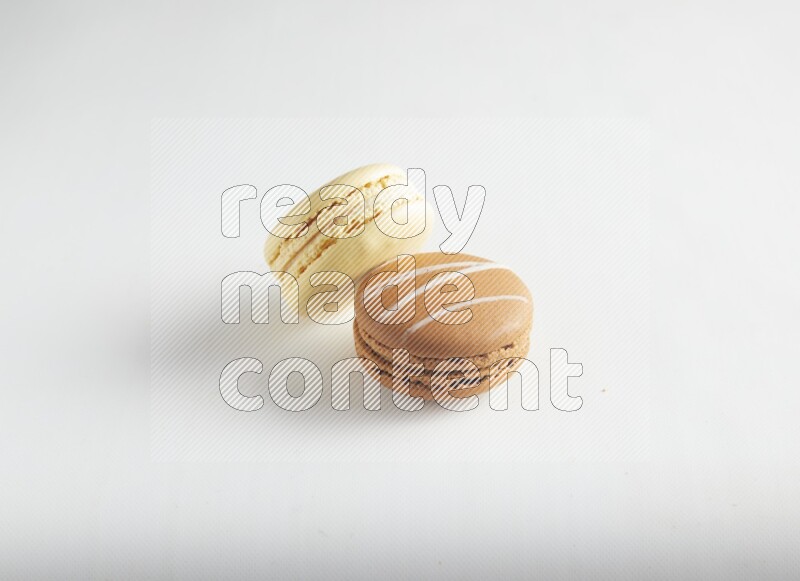 45º Shot of of two assorted Brown Irish Cream, and Yellow Vanilla macarons on white background