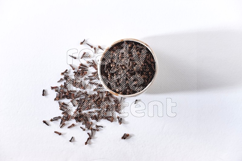 A beige ceramic bowl full of cloves on a white flooring